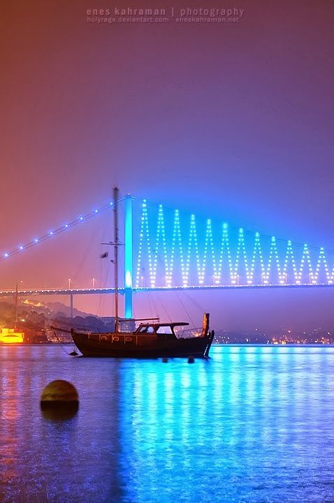 a boat floating on top of a body of water next to a bridge at night