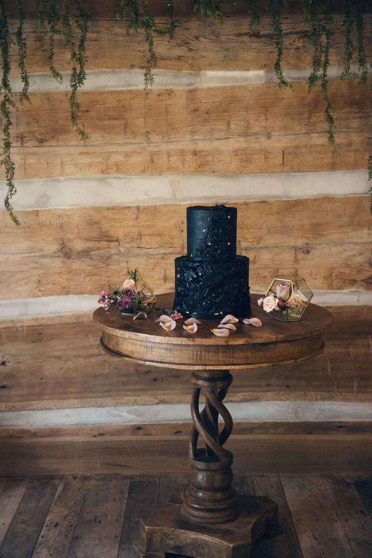 a black wedding cake sitting on top of a wooden table next to a wood wall