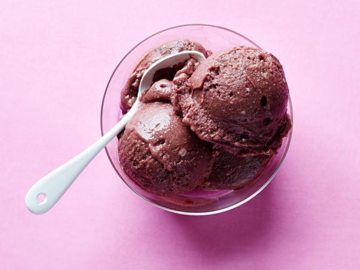 two scoops of ice cream in a glass bowl on a pink surface with a spoon