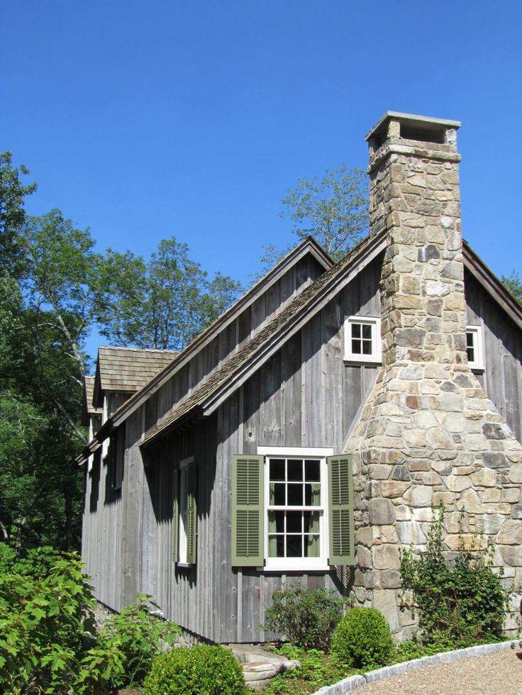 an old stone house with green shutters on the windows and a chimney in front