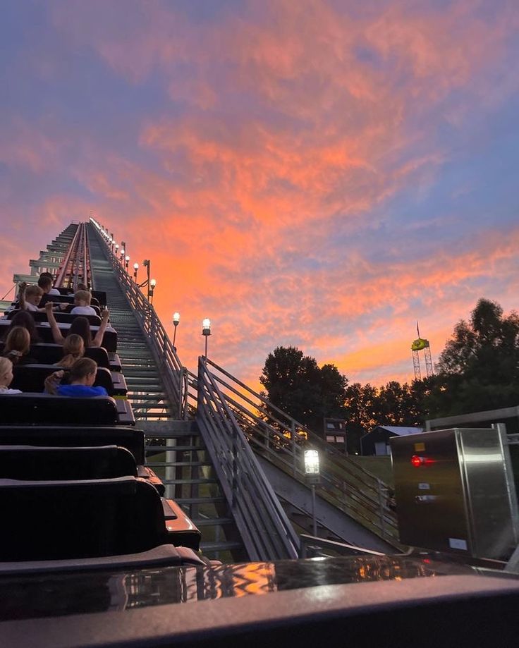 people sitting on the top of a roller coaster at sunset or sunrise with pink clouds