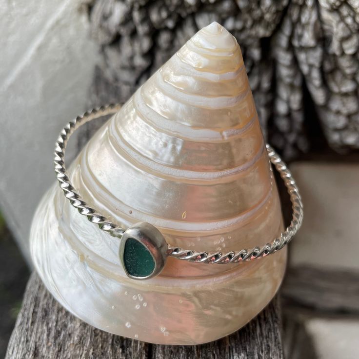 a silver bracelet with a green stone on it sitting on top of a wooden table