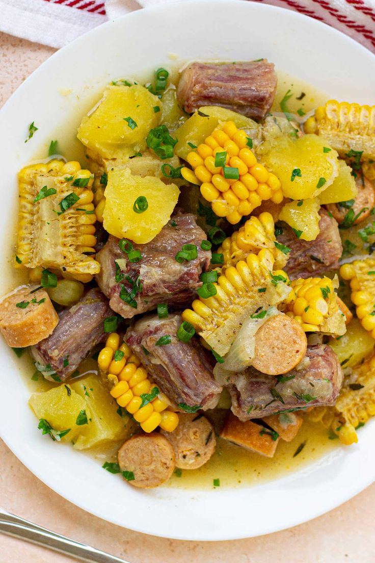 a white bowl filled with corn on the cob and potatoes next to a fork