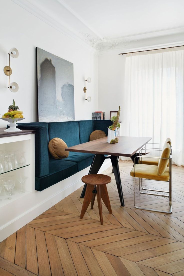 a dining room table and chairs in front of a blue couch with an art work on the wall