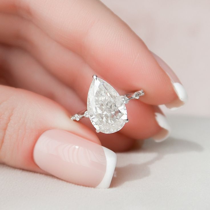 a woman's hand holding a ring with a pear shaped diamond on top of it