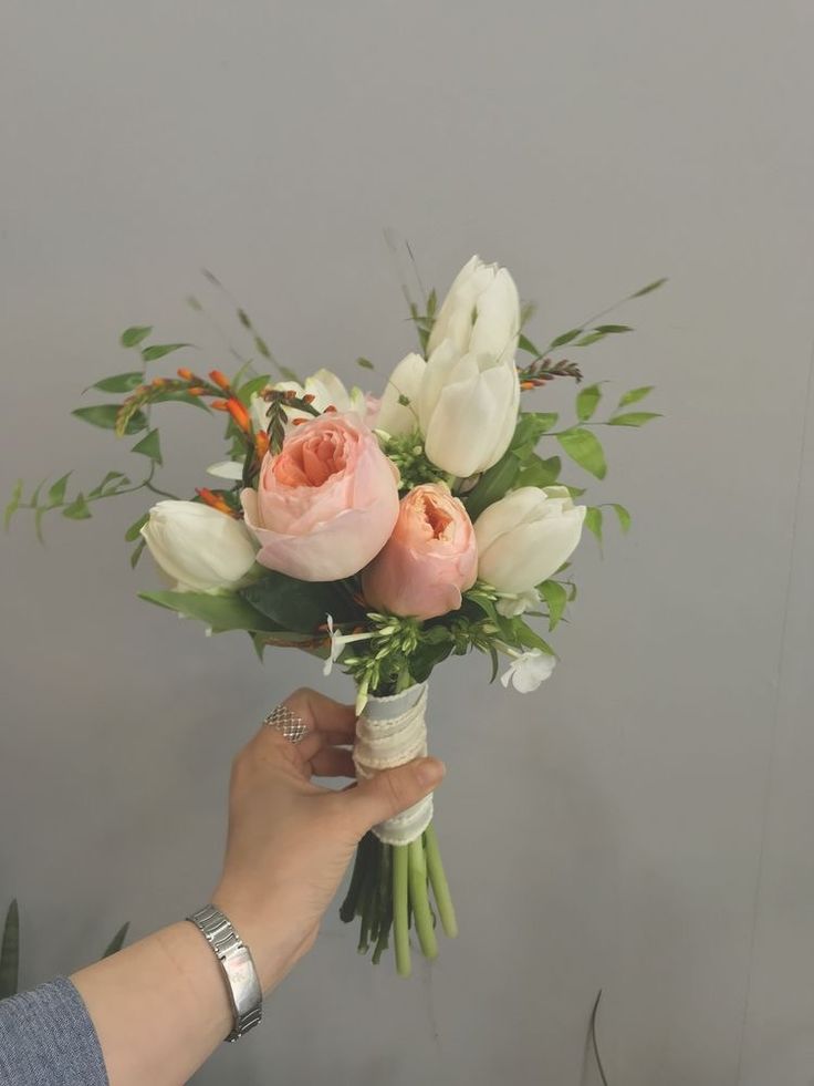 a person holding a bouquet of flowers in front of a gray wall with greenery