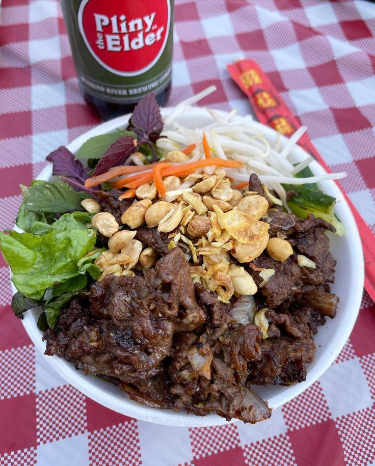 a white plate topped with meat and veggies next to a bottle of beer