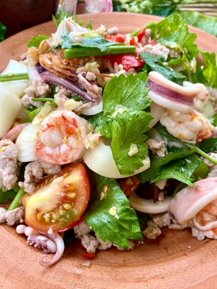 a salad with shrimp, tomatoes and lettuce on a wooden plate at an outdoor table