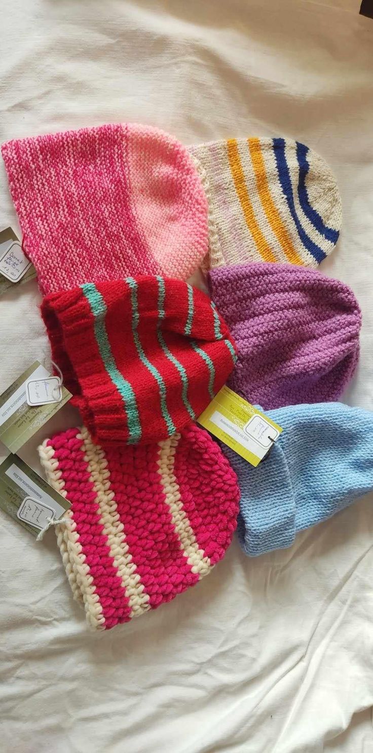 four knitted mittens laid out on top of a white sheet with tags attached to them