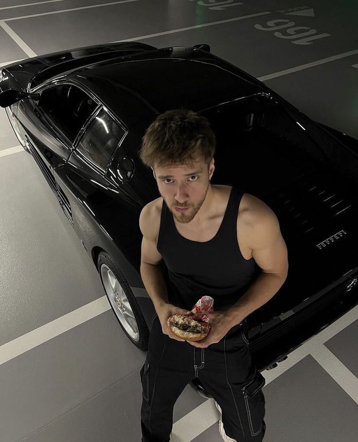 a man standing in front of a car holding a sandwich