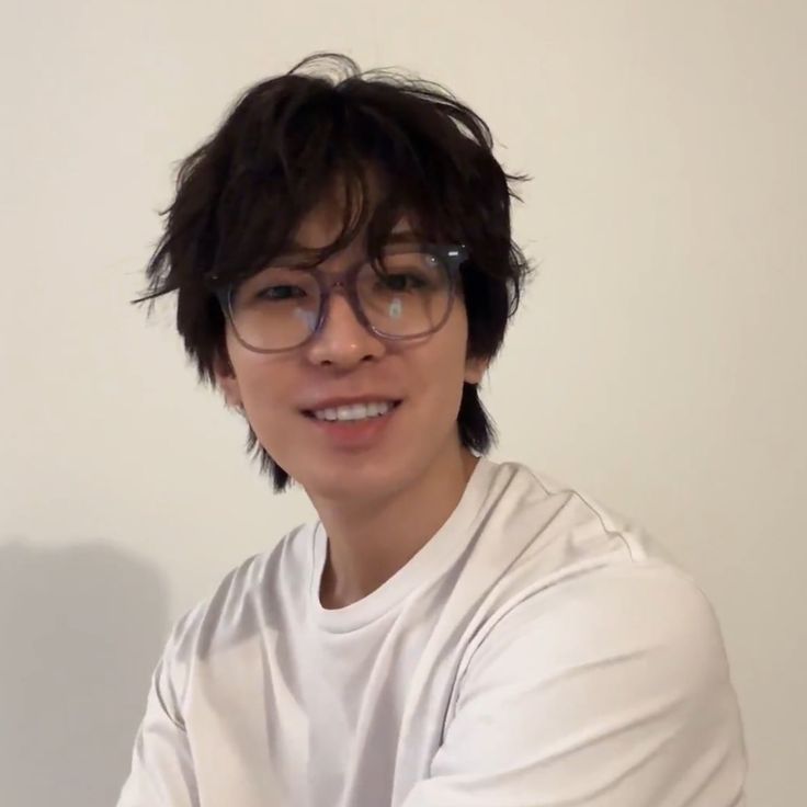 a young man with glasses is smiling for the camera while wearing a white shirt and black rimmed glasses