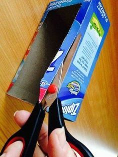 someone holding scissors in front of a box that is open and ready to cut it