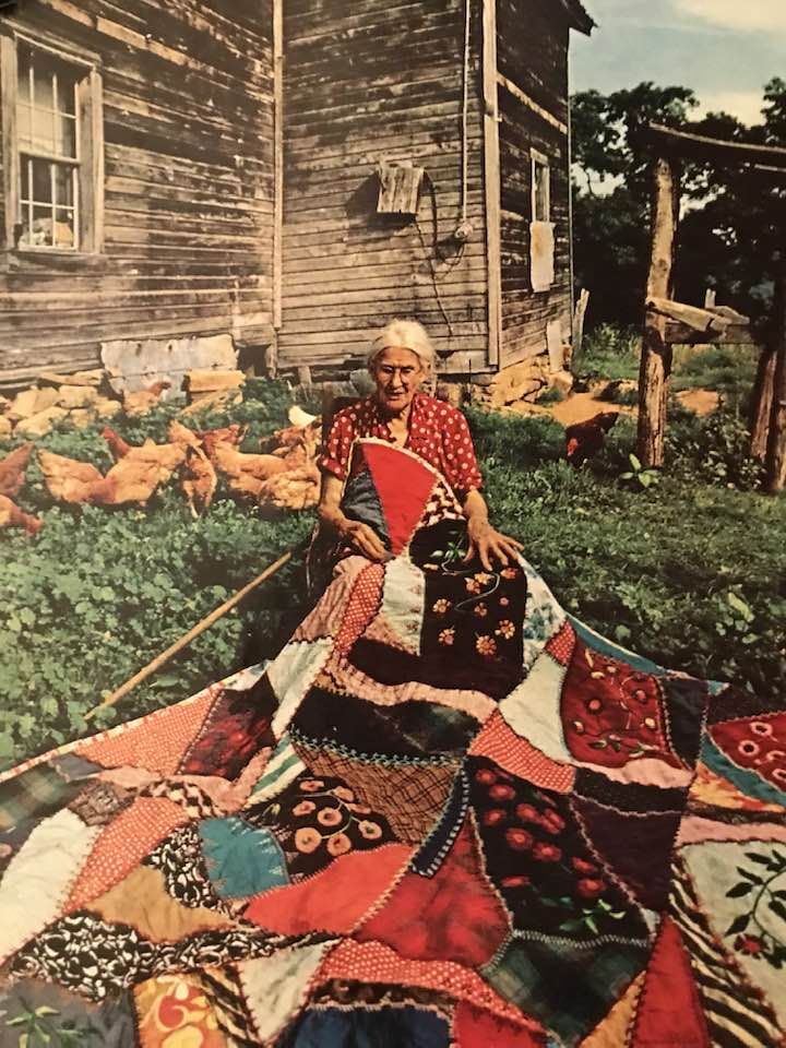 an old woman sitting in front of a quilt