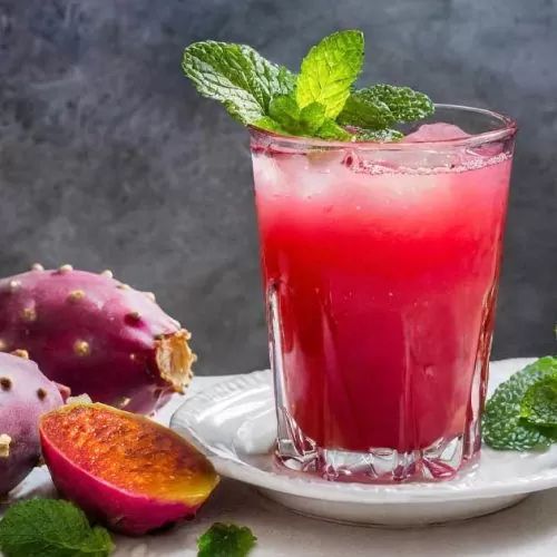 a glass filled with liquid next to some fruit on a white plate and green leaves