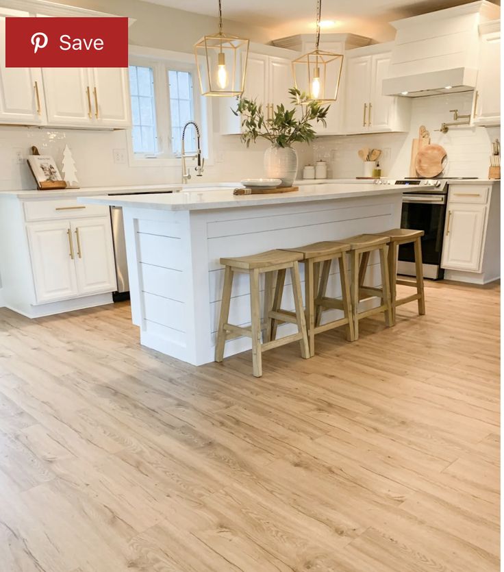 a large kitchen with white cabinets and wooden flooring is pictured in this image, there are two stools on the center island