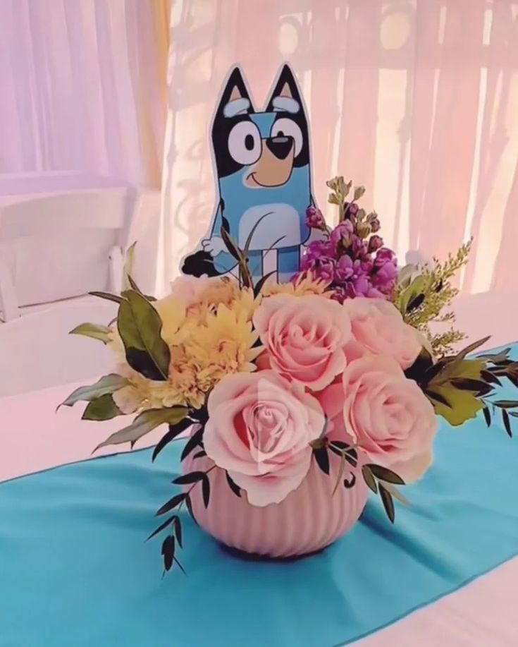 a pink vase filled with flowers on top of a blue table cloth covered tablecloth