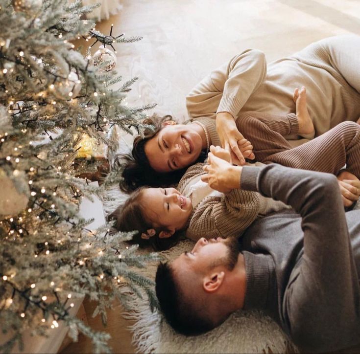 two people laying on the floor next to a christmas tree