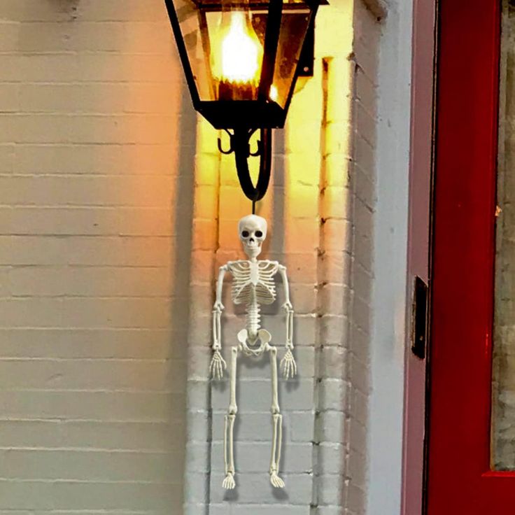 a skeleton hanging from the side of a wall next to a red door with a light on it