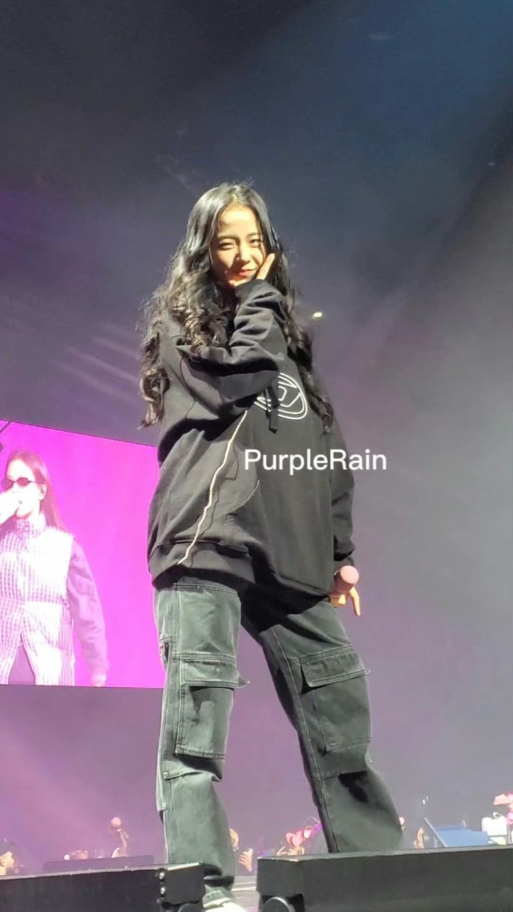 a woman standing on top of a stage with her hands in her pockets and looking at the camera