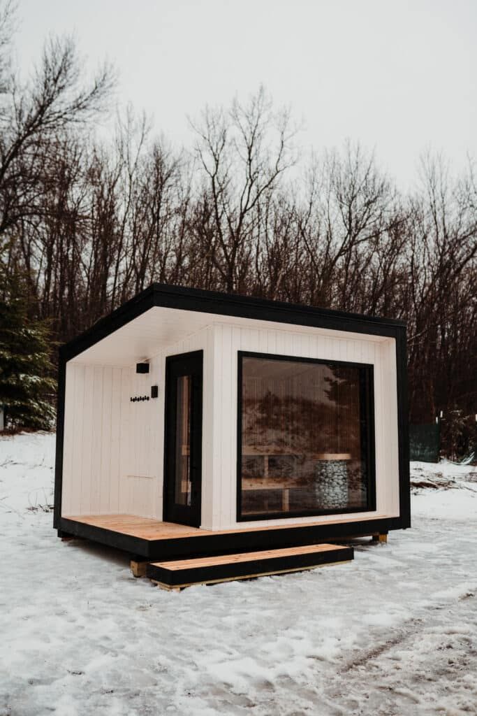 a small white and black cabin sitting on top of snow covered ground