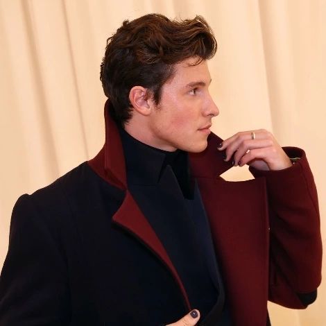 a man in a black and red jacket is holding his coat over his shoulder while looking off to the side