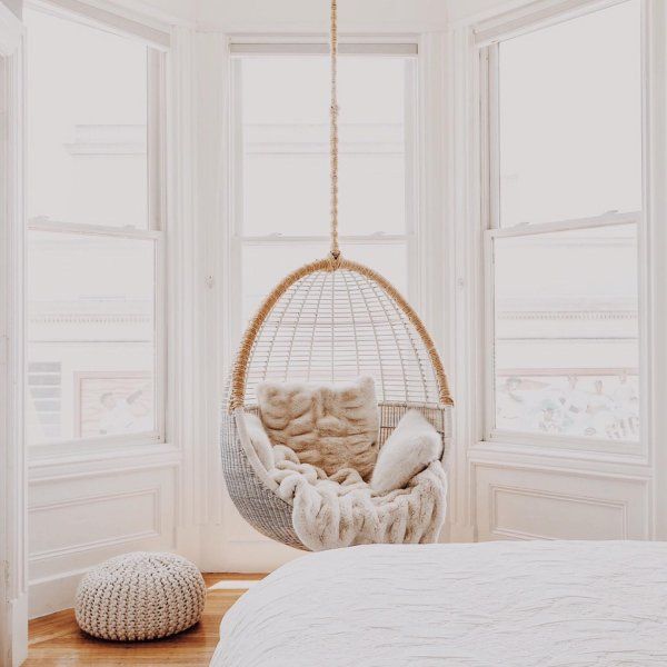 a bedroom with a bed, window and hanging chair in the middle of the room