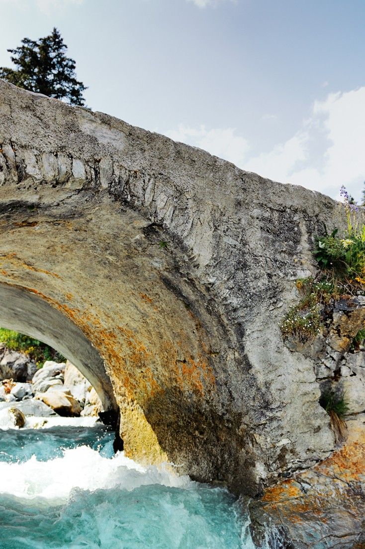 a large stone bridge over a river next to a forest