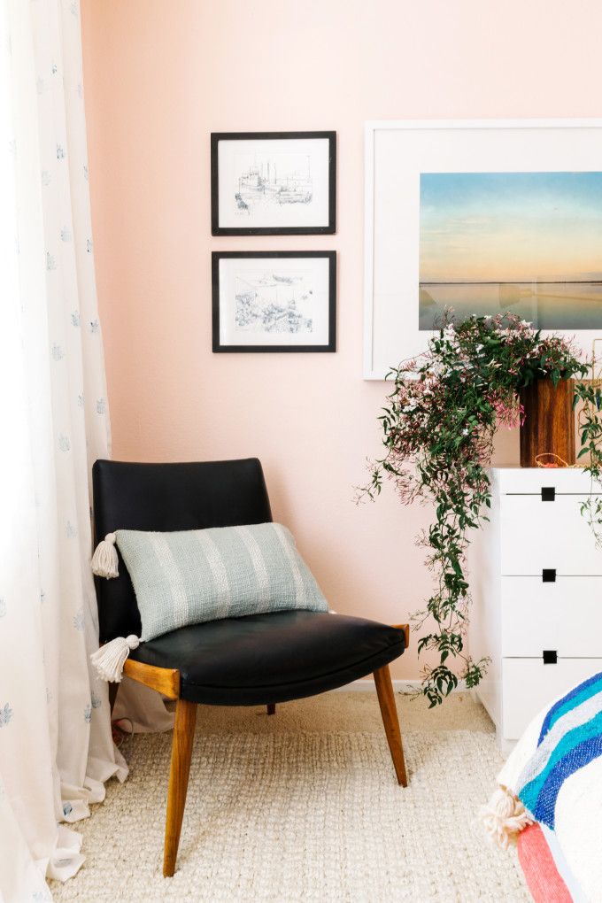 a bedroom with pink walls and pictures on the wall, including a black chair in front of a white dresser