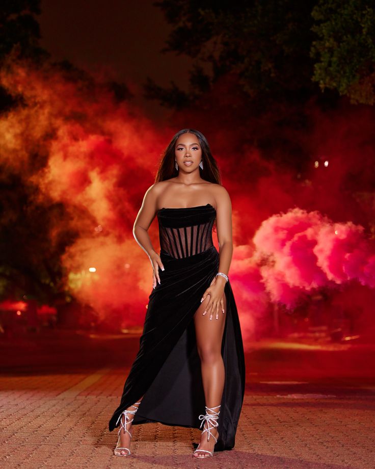 a woman in a black dress posing for the camera with fireworks behind her and trees