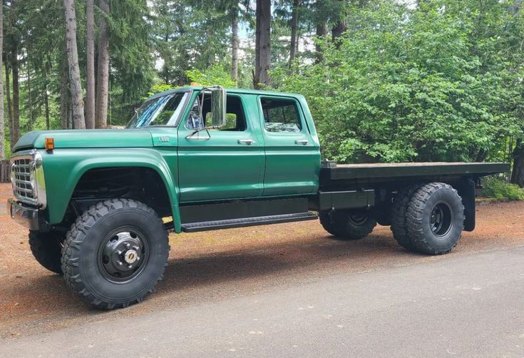 a green pick up truck parked on the side of a road in front of trees