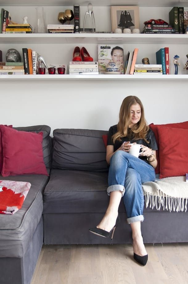 a woman sitting on top of a gray couch next to a book shelf filled with books