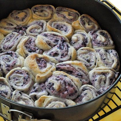 a pan filled with blueberry rolls sitting on top of a yellow tablecloth next to an oven