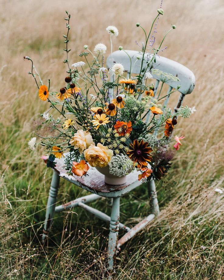 a bouquet of flowers sitting on top of a wooden chair in the middle of a field