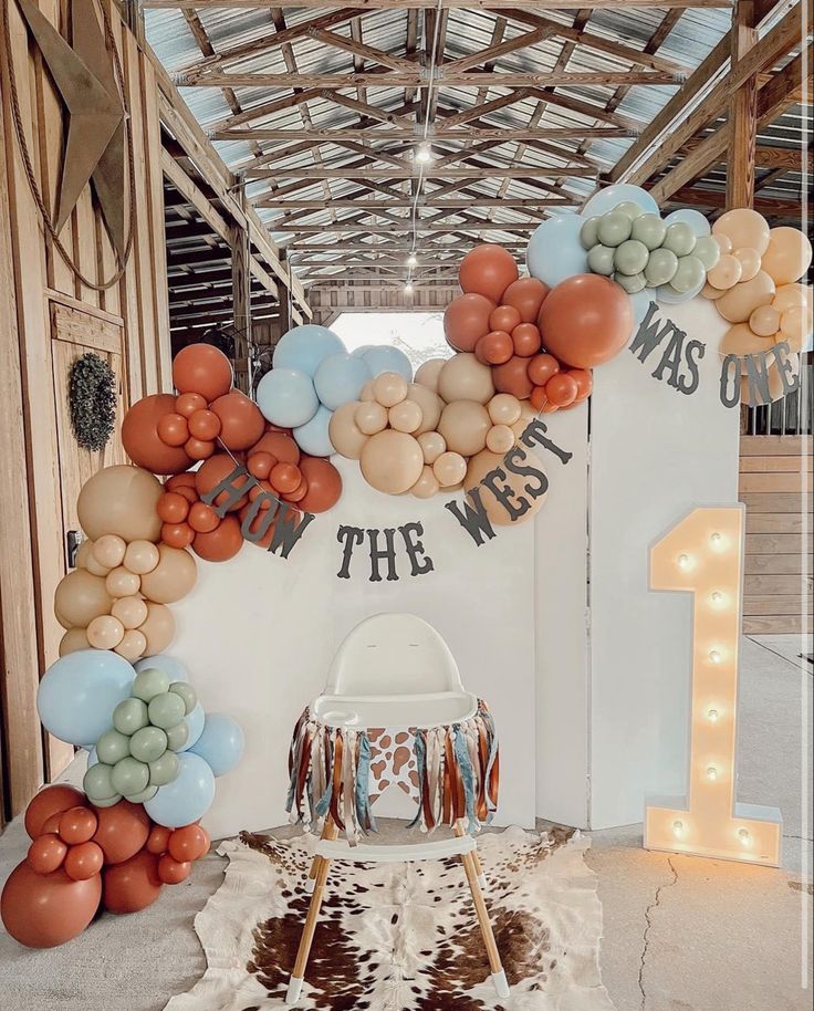 balloons are hanging from the ceiling in front of a white chair and cowhide rug