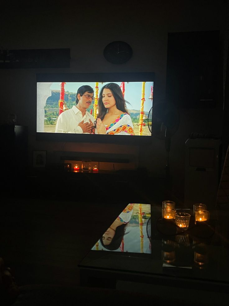 a man and woman sitting in front of a flat screen tv with candles on the table