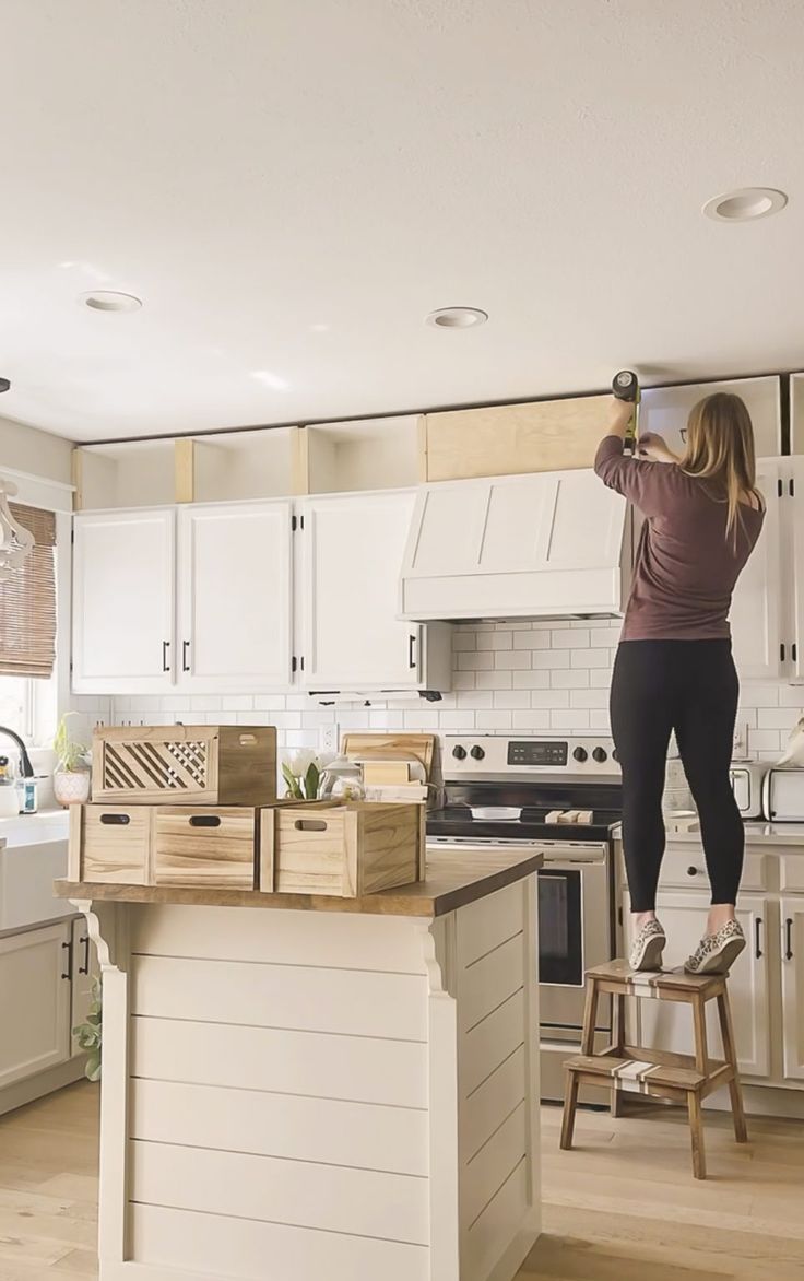 a woman standing on top of a kitchen counter next to a wooden stool in front of an oven