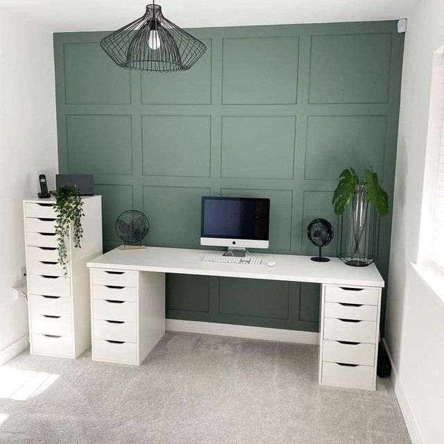 a white desk with a computer on top of it in front of a green wall