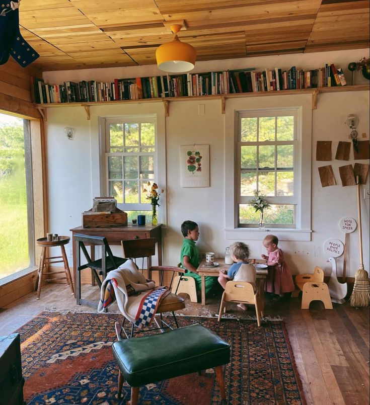 two children sit in chairs and play with books on the shelves above them, while another child sits at a table