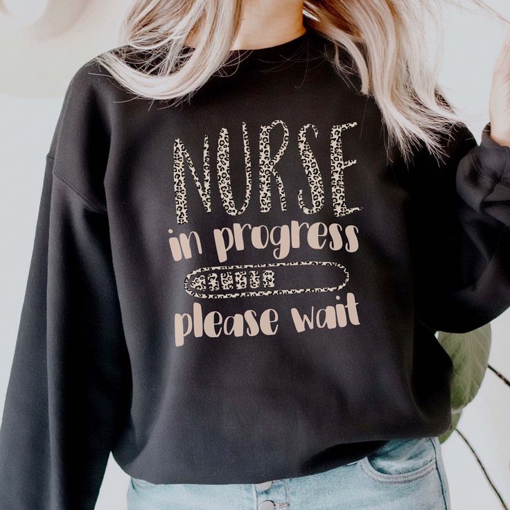 a woman with blonde hair wearing a black sweatshirt that says nurse in progress please wait