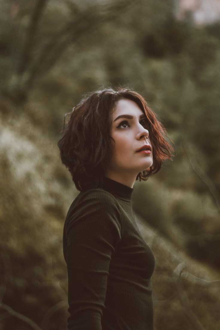 a woman standing in the woods with her head turned to the side, looking off into the distance