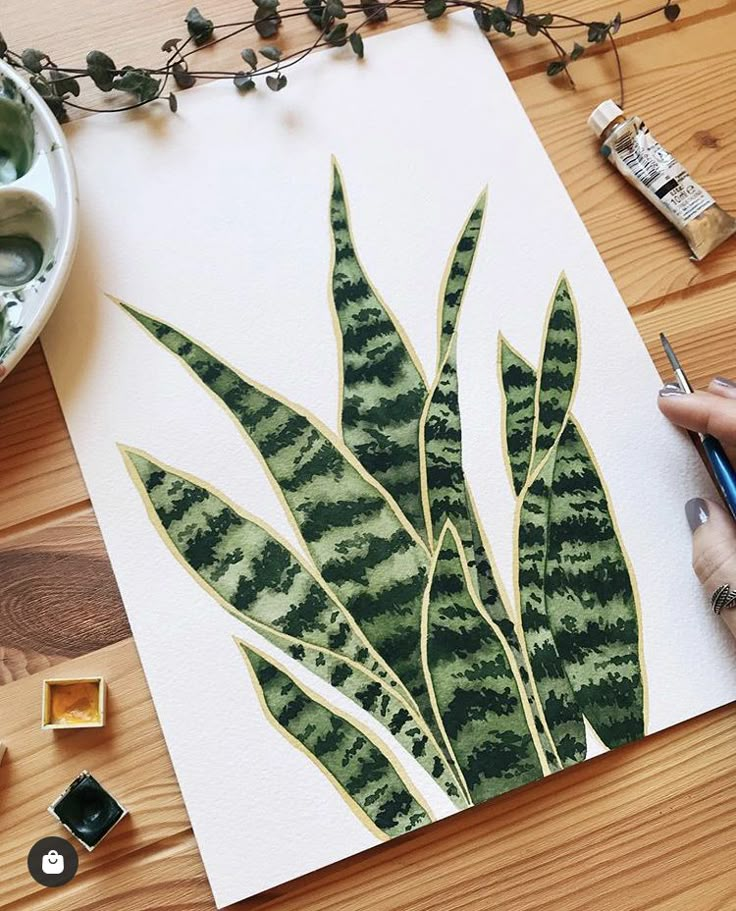 a person is painting a green plant with watercolors on white paper and surrounded by greenery