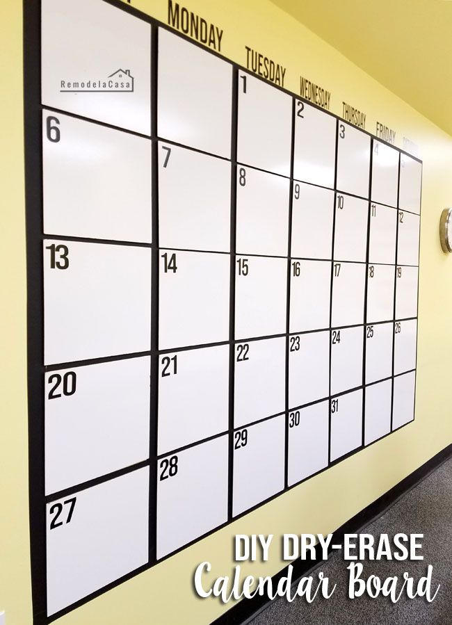 a dry erase calendar hanging on the wall in an office space with yellow walls and carpet