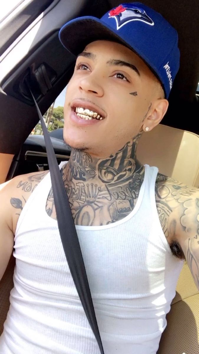 a man with tattoos sitting in the back seat of a car wearing a blue hat