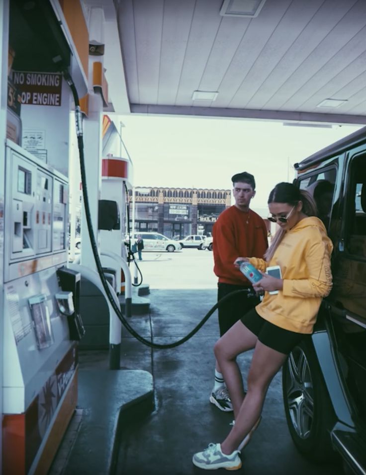 a man and woman are filling up their cars at a gas station