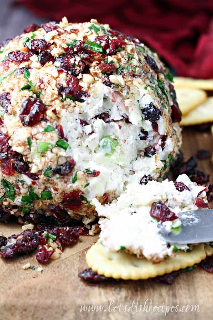 a cheese ball with cranberries and other toppings on it next to crackers