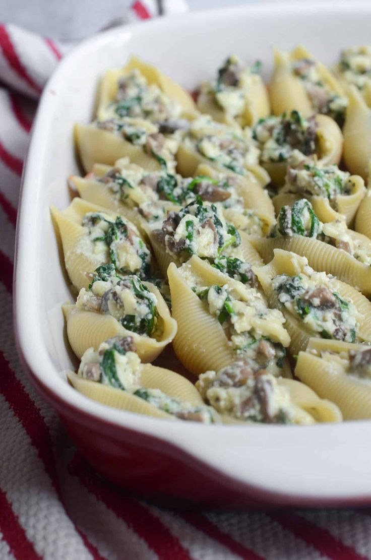 a casserole dish filled with pasta and spinach on a red and white towel