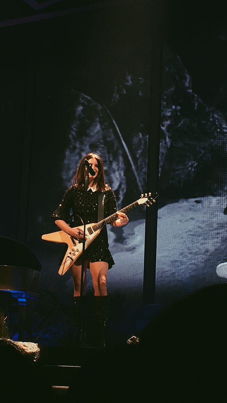 a woman standing on top of a stage holding a guitar