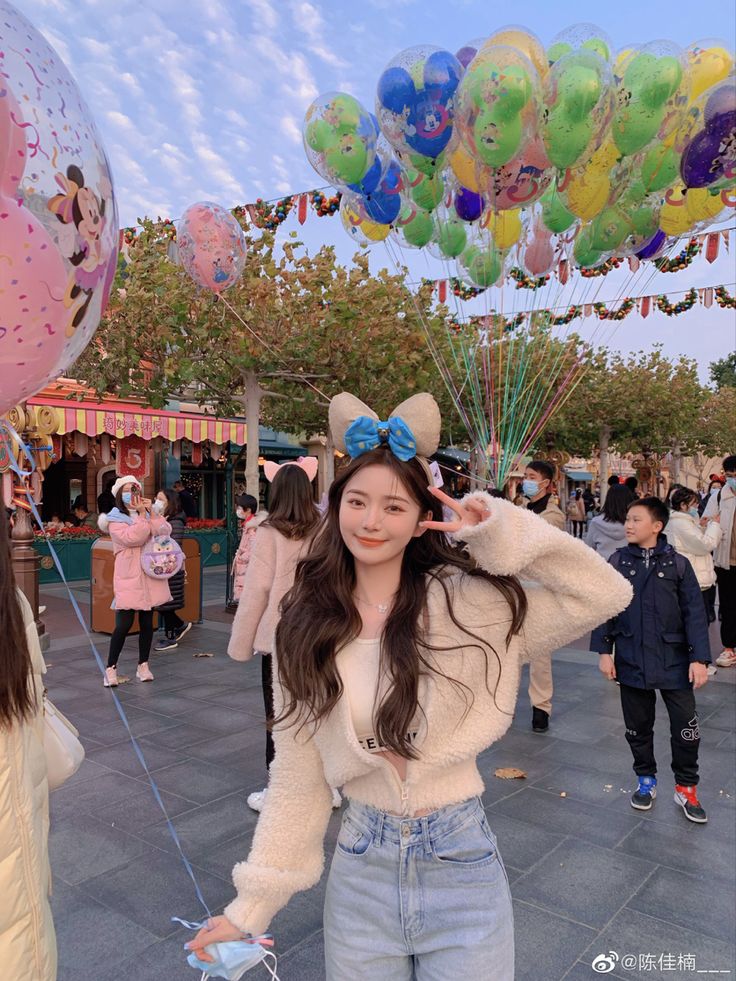 a woman standing in front of balloons and other people at an amusement park with her hands on her head