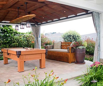 a pool table sitting on top of a patio next to a wooden bench and potted plants