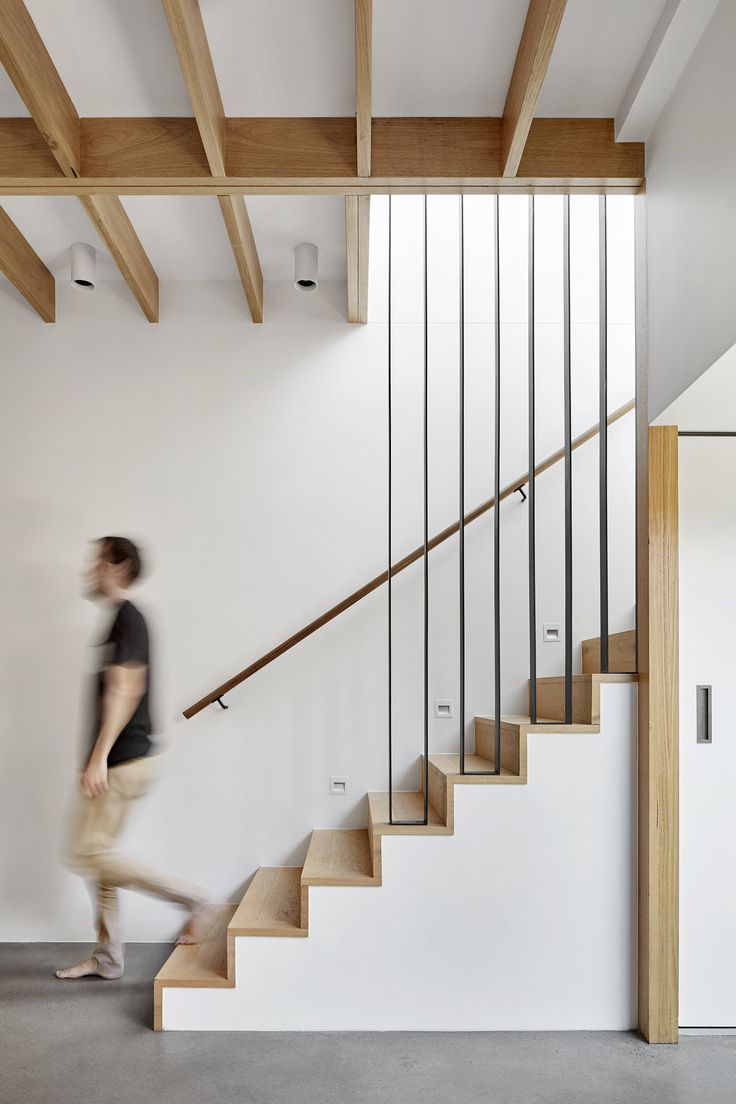 a man is walking down the stairs in a modern house with white walls and wood beams